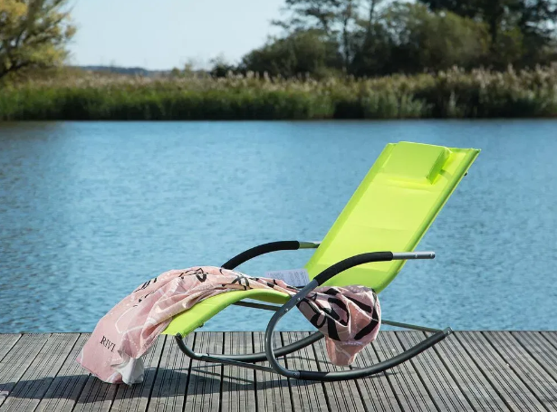 Odabir vrtnog namještaja - Svijetlozelena ležaljka za opuštanje s ručnikom na drvenom pristaništu uz jezero ili rijeku.