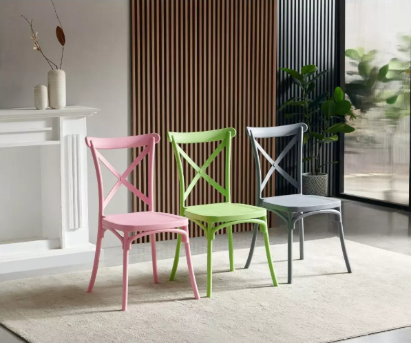 Tri stolice u stilu Thonet stolica s križnim naslonom, u ružičastoj, svijetlozelenoj i tamno sivoj boji, postavljene na tepihu ispred drvenog panela i biljke.