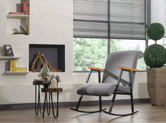 Sigurnost i stabilnost namještaja: Moderan interijer s baršunastom, svijetlo sivom stolicom za ljuljanje, crnim žaluzinama, ugrađenim kaminom i police na zidu.